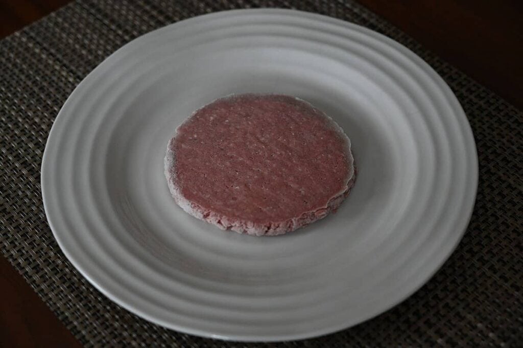 Top down image of one frozen lean ground beef patty served on a plate. 