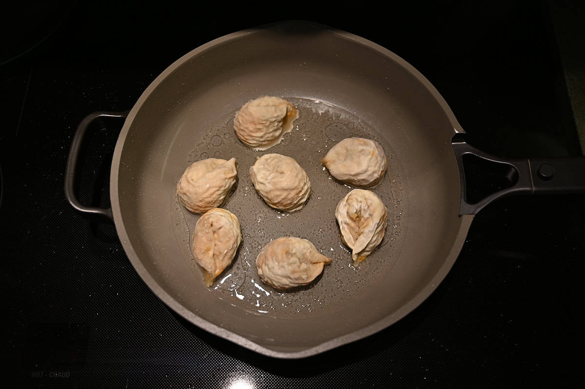 Image of seven dumplings being cooked in a pan on a stovetop.