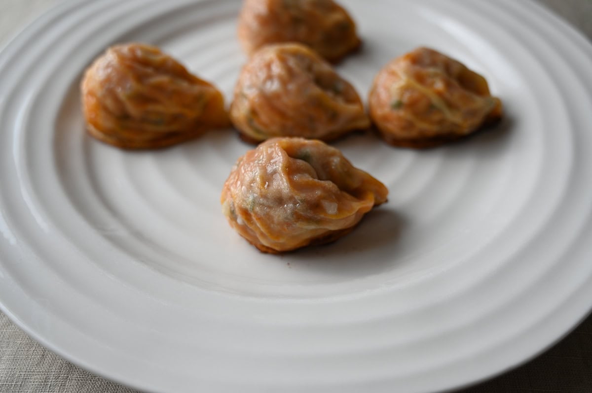 Closeup side view image of five cooked dumplings sitting on a white plate. 