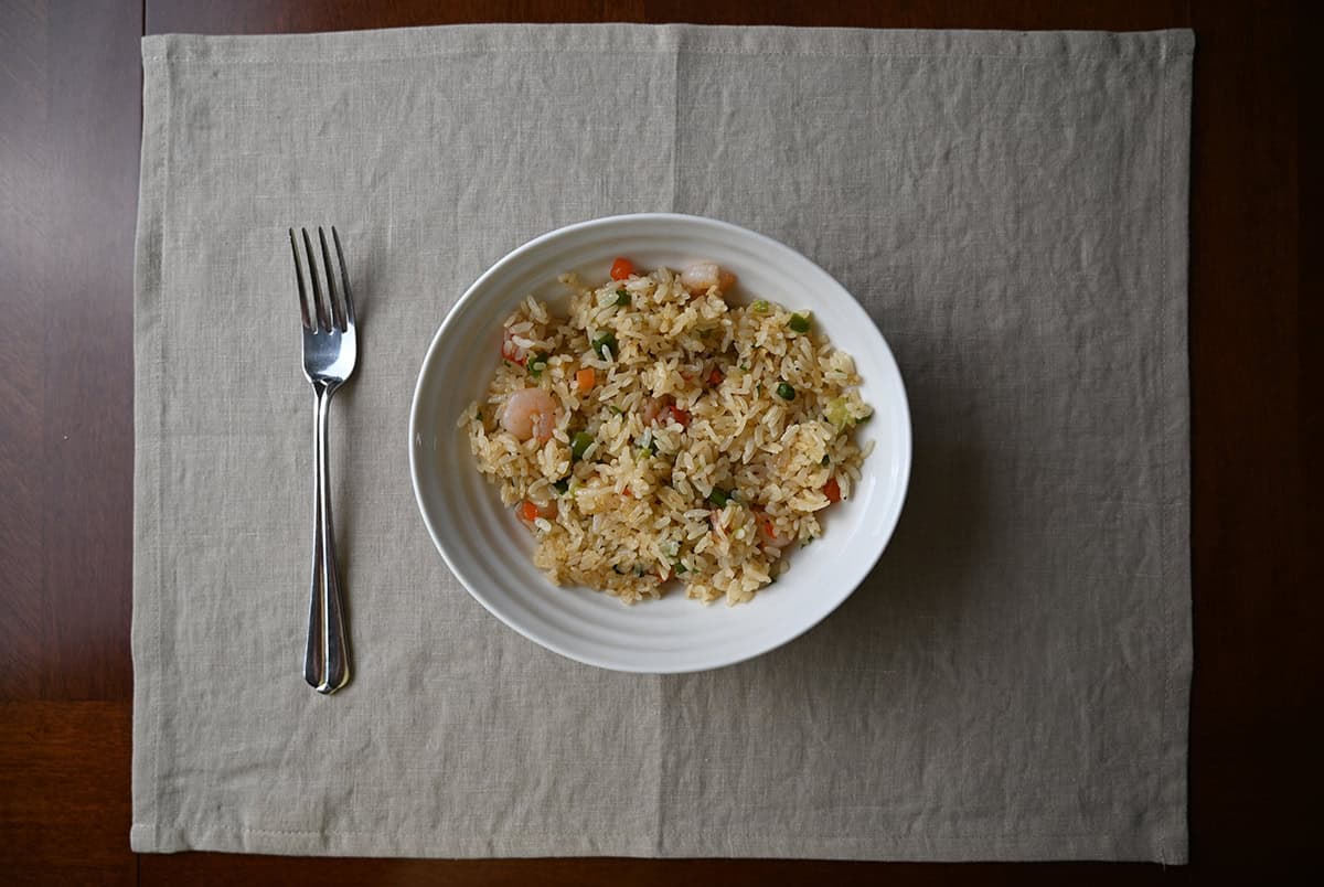 Top down image of a bowl of shrimp fried rice beside a fork, 