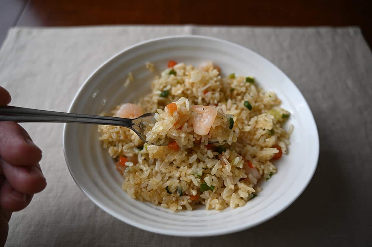 Top down closeup image of a bowl of shrimp fried rice with a fork hovering over the bowl with a forkful of rice and shrimp.