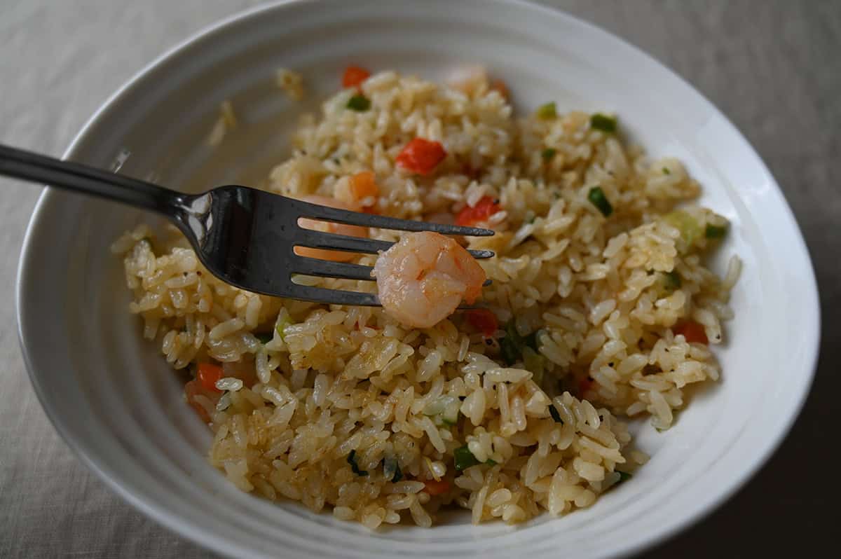 Closeup image of a fork with one small shrimp on it hovering over a bowl of shrimp fried rice.