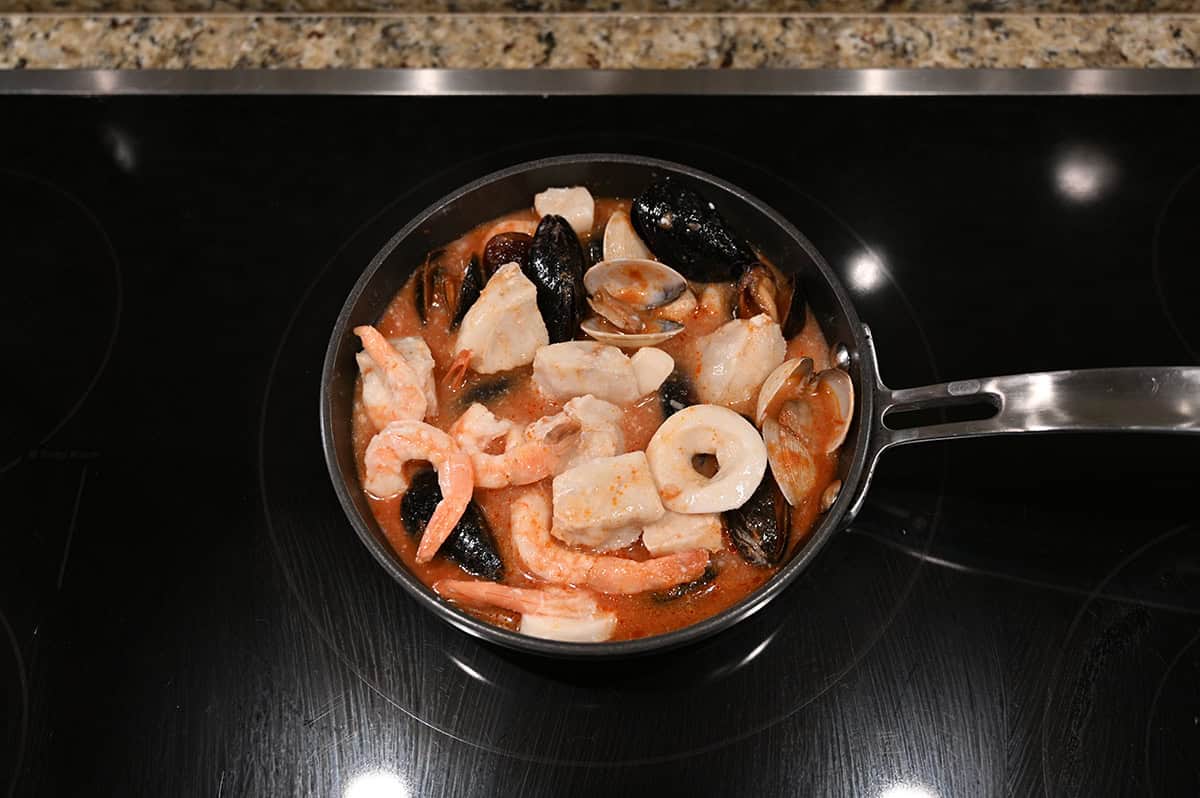 Top down image of the cioppino cooking in a frying pan on a stovetop.