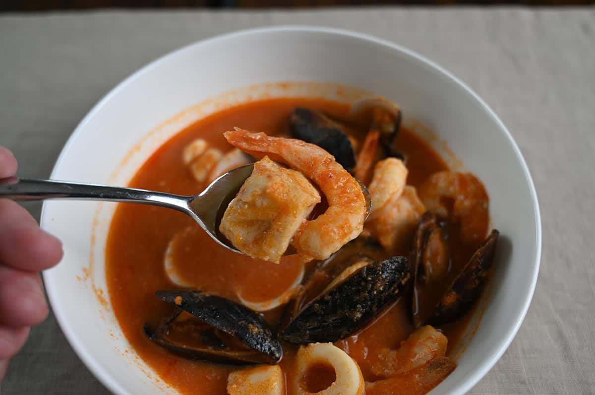 Closeup image of a spoon of cioppino hovering over the bowl of it. There is shrimp and fish on the spoon.