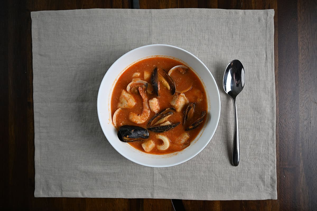 Top down image of a bowl of cioppino on a placemat with a spoon sitting beside the bowl. 