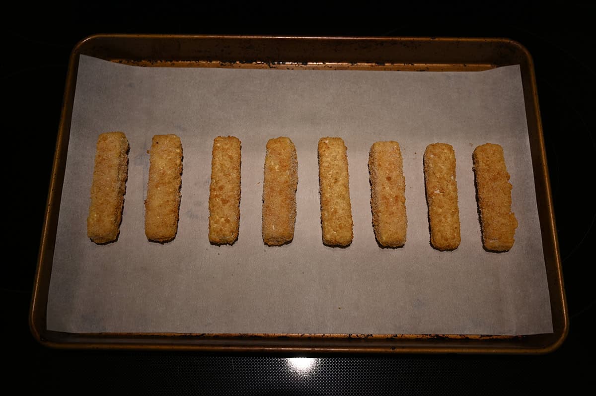 Image of eight fish sticks on a baking pan about to be cooked in the oven.