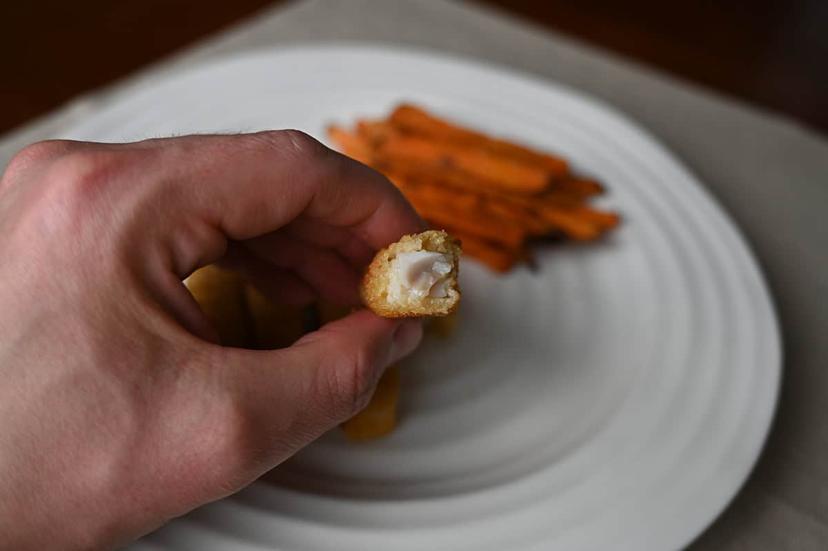 Image of a hand holding one fish stick with a bite taken out of it so you can see the center of the fish stick.