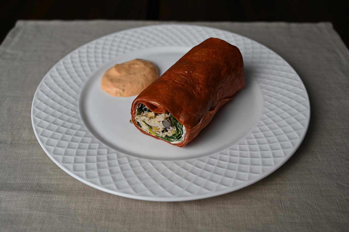 Sideview closeup image of one wrap served on a white plate beside a dollop of sauce.