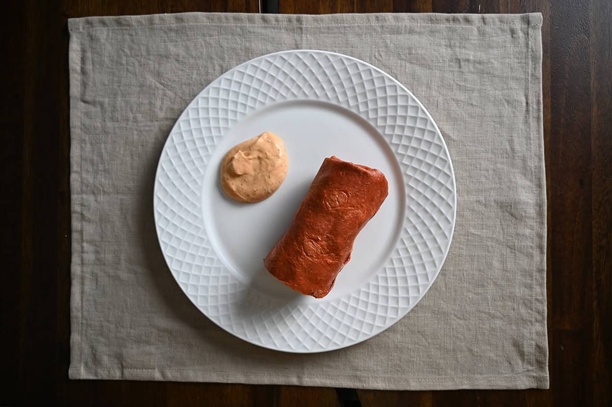 Top view image of a southwest chicken wrap served on a white plate beside some sauce.