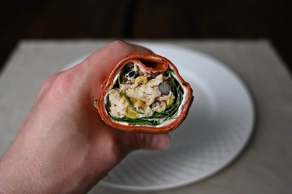 Closeup image of a hand holding one wrap showing the filling in the wrap like chicken, black beans, corn. 