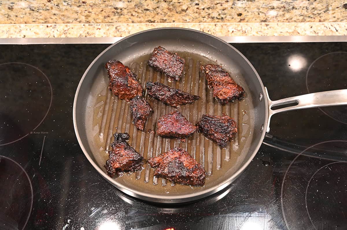 Top down image of brisket burnt ends being heated in a frying pan on the stove.