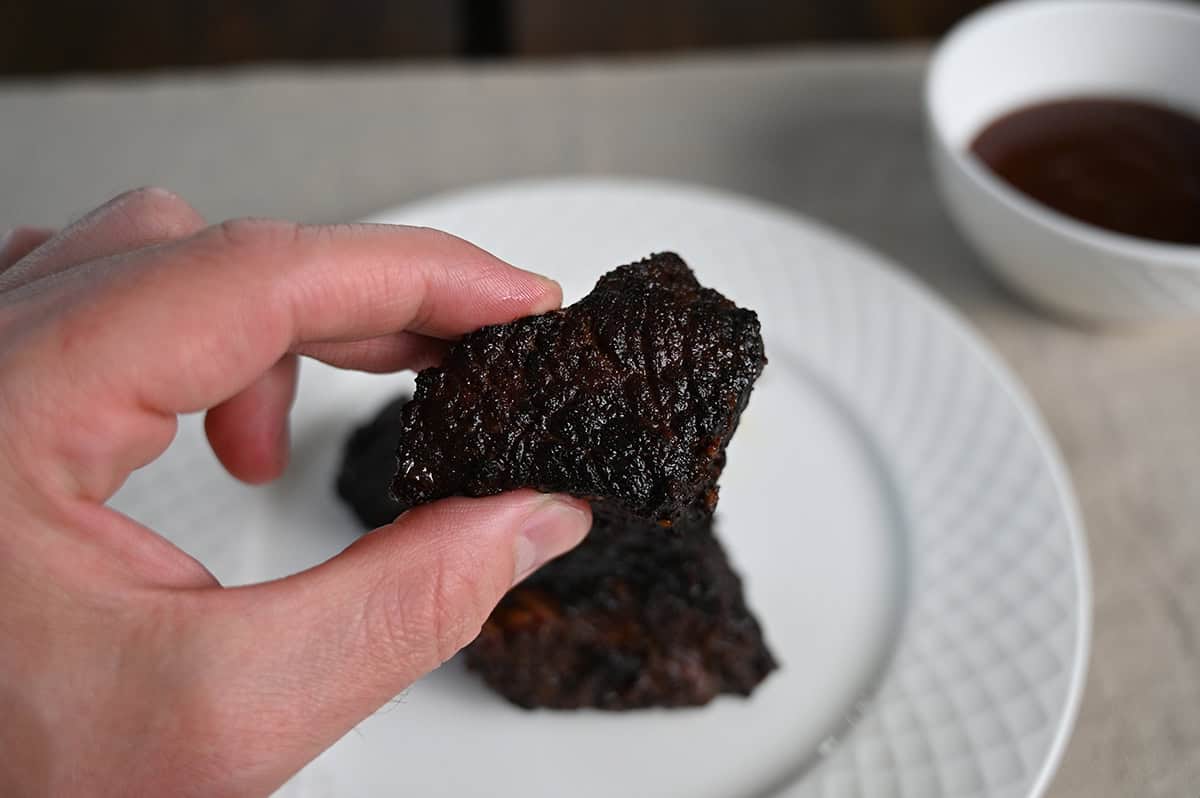 Image of a hand holding one brisket burnt end up close to the camera without barbecue sauce on it.