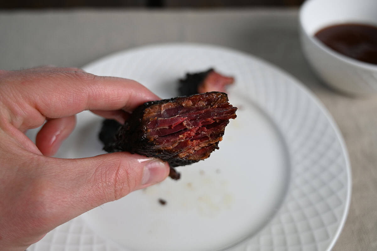 Image of a hand holding one brisket burnt end close to the camera with a bit of barbecue sauce on it.