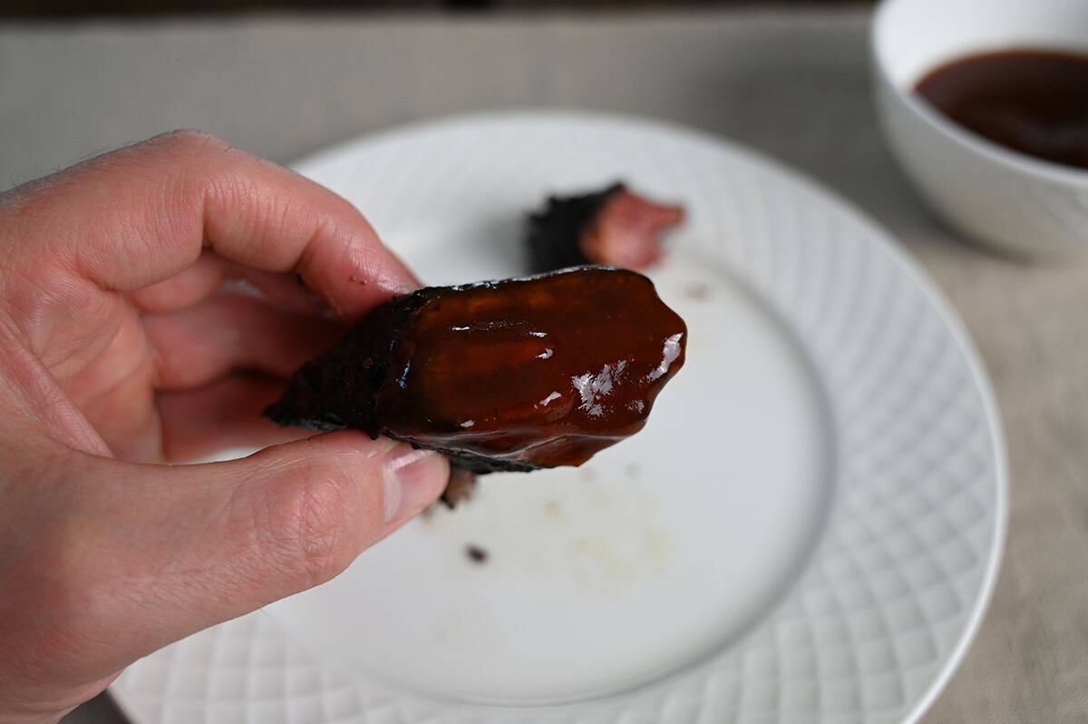 Image of a hand holding one brisket burnt end close to the camera with barbecue sauce on it.