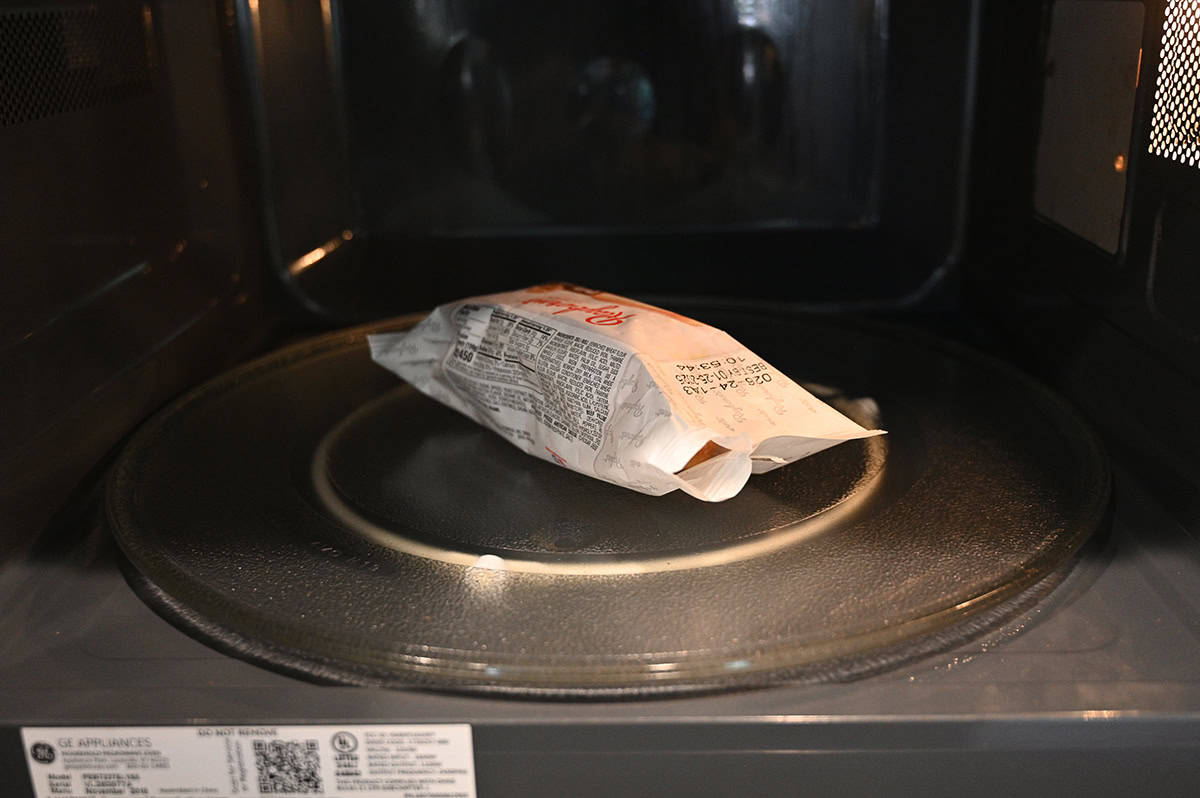 Image of one Philly cheesesteak being microwaved in it's plastic package with the plastic opened slightly.