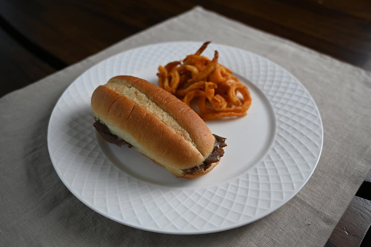 Top down image of a philly cheesesteak served on a white plate beside some fries.