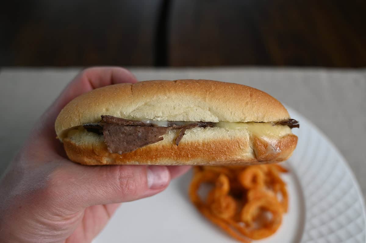 Image of a hand holding one philly cheesesteak sandwich close to the camera you can see cheese and meat inside the bread.