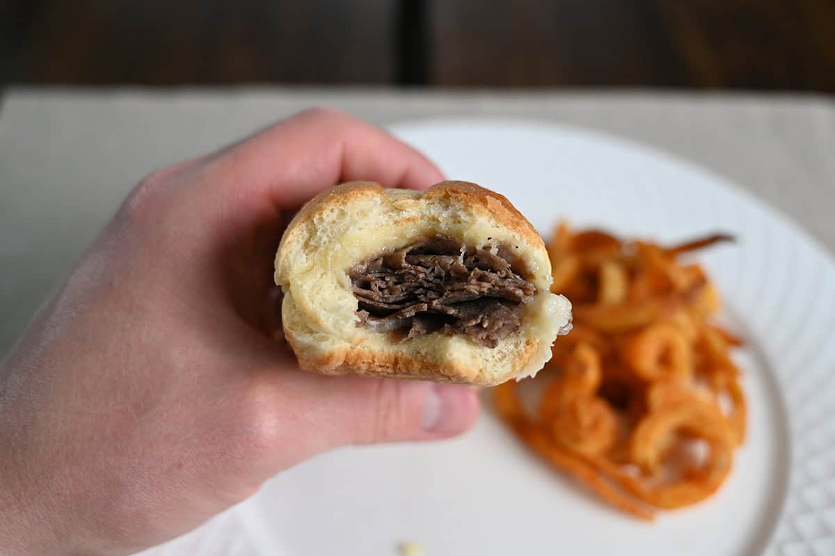 Image of a hand holding one philly cheesesteak sandwich close to the camera with a few bites taken out of it so you can see the filling.