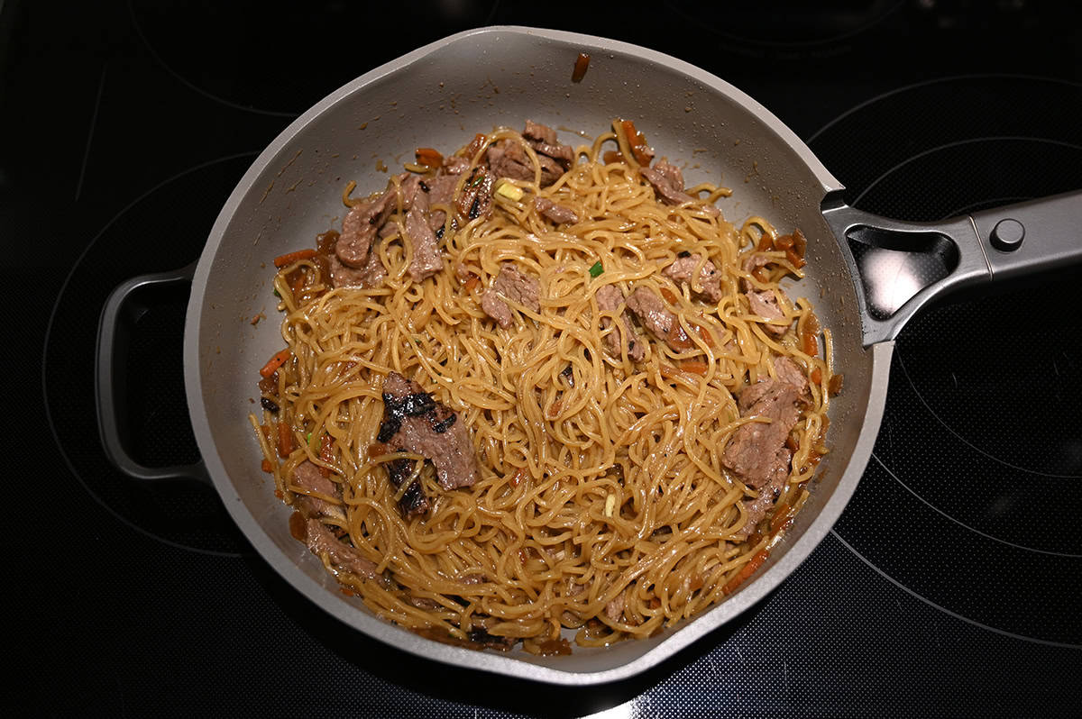 Top down image of a pan on a stovetop cooking a beef noodle stir fry.