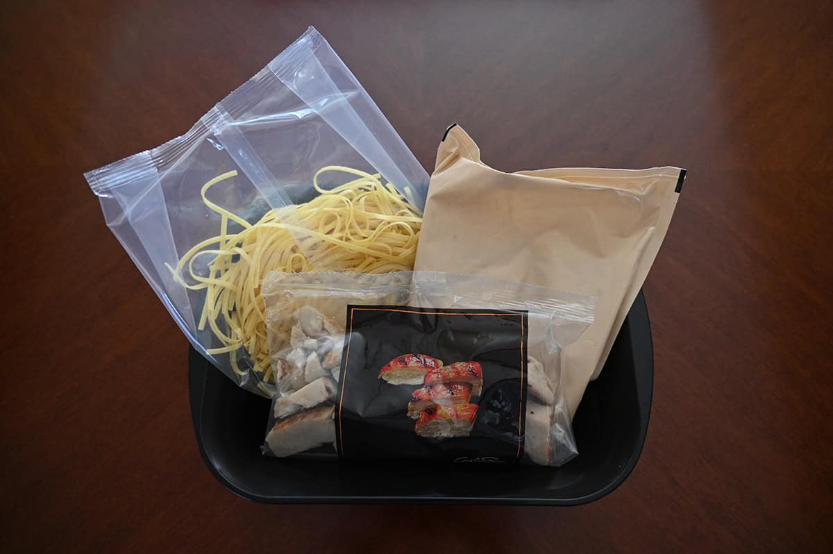 Image of a plastic container with a bag of noodles, a bag of sauce and a bag of chicken and vegetables in it showing everything that comes in the package. 