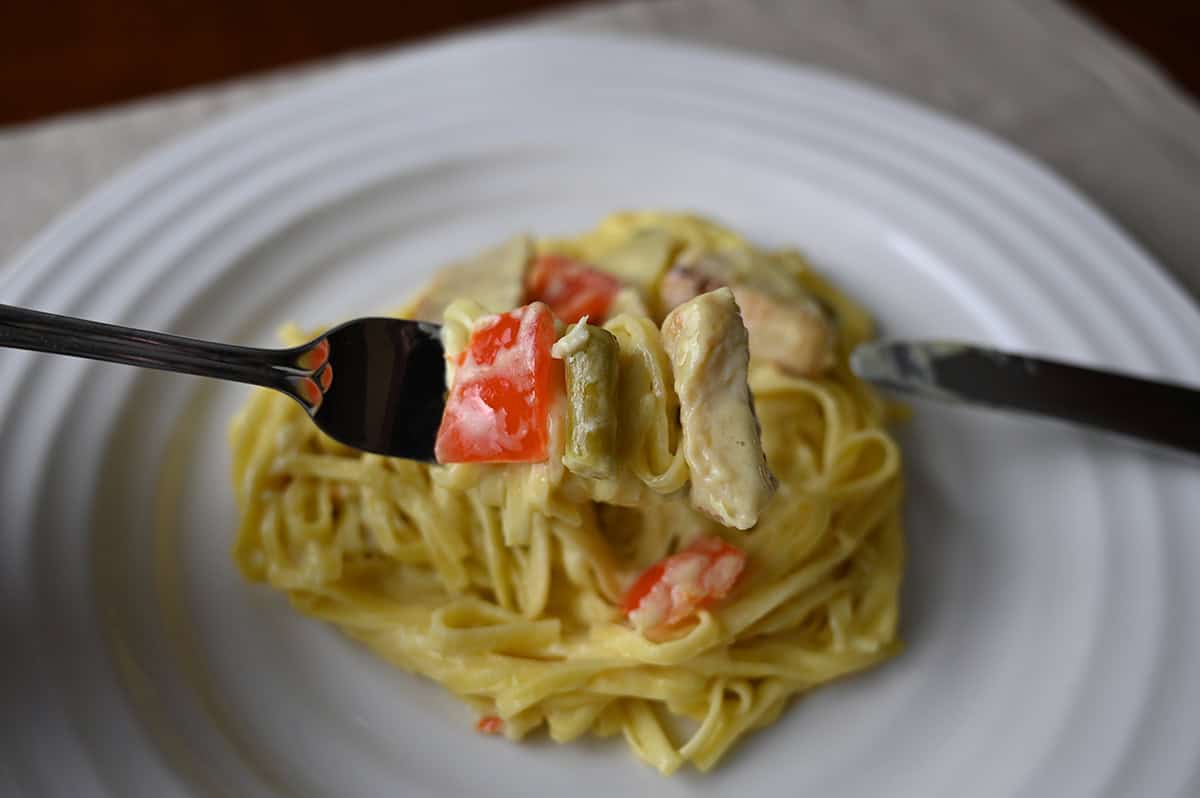 Closeup image of a fork with chicken, pasta and vegetables on it hovering over a plate of pasta.