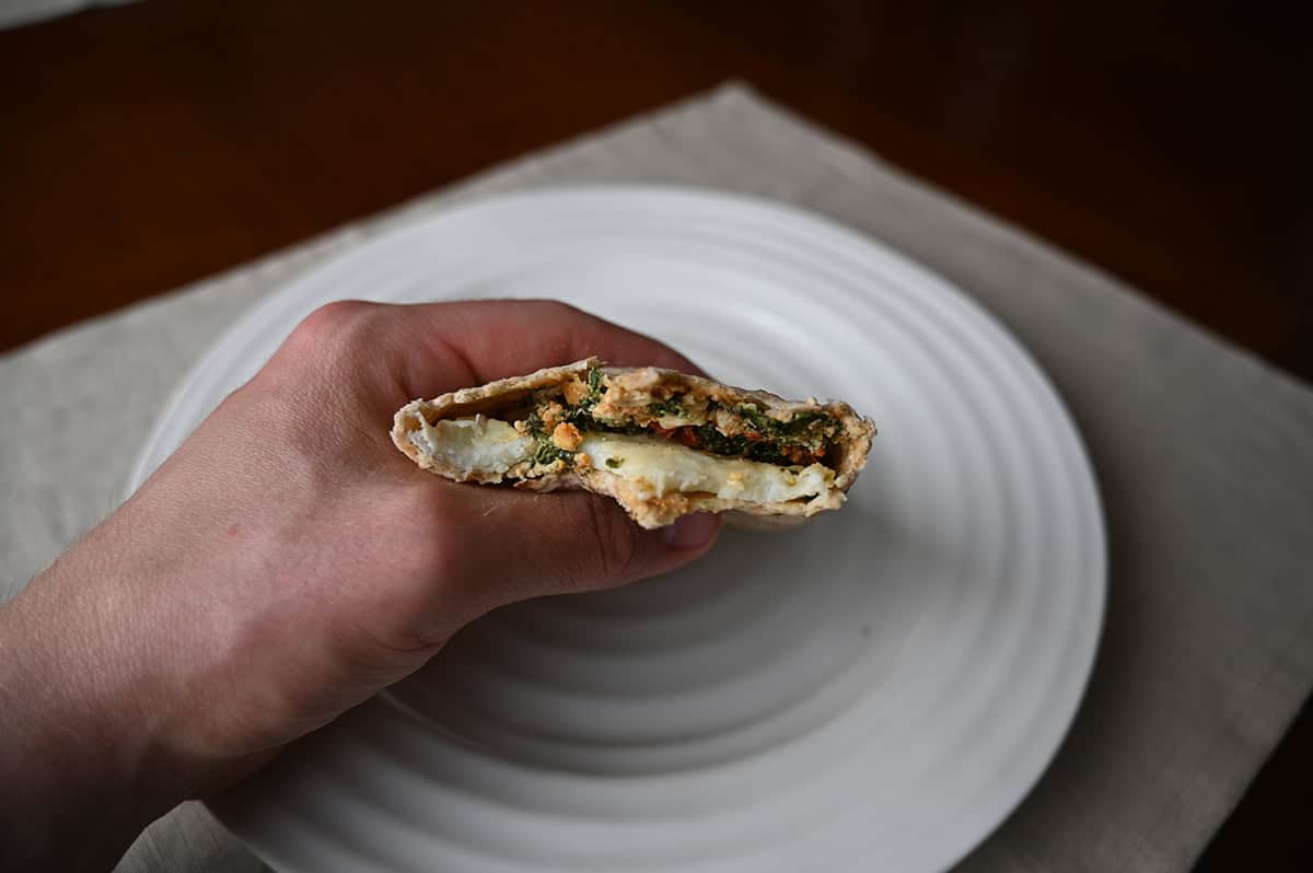 Sideview closeup image of a hand holding one breakfast wrap with a few bites taken out if so you can see the filling.