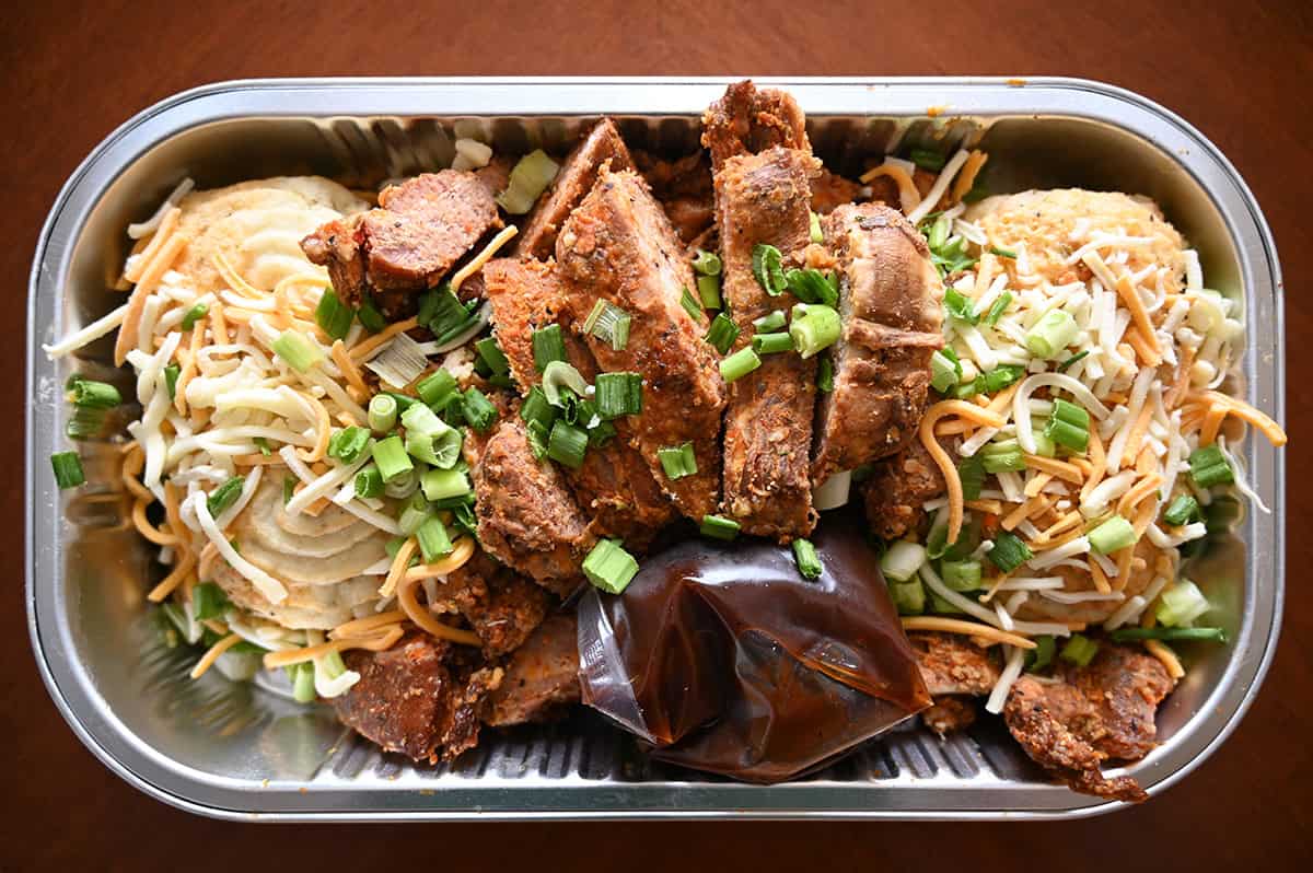 Top down image of the ribs ends and baked potatoes container with the lid off sitting on a table before being cooked.