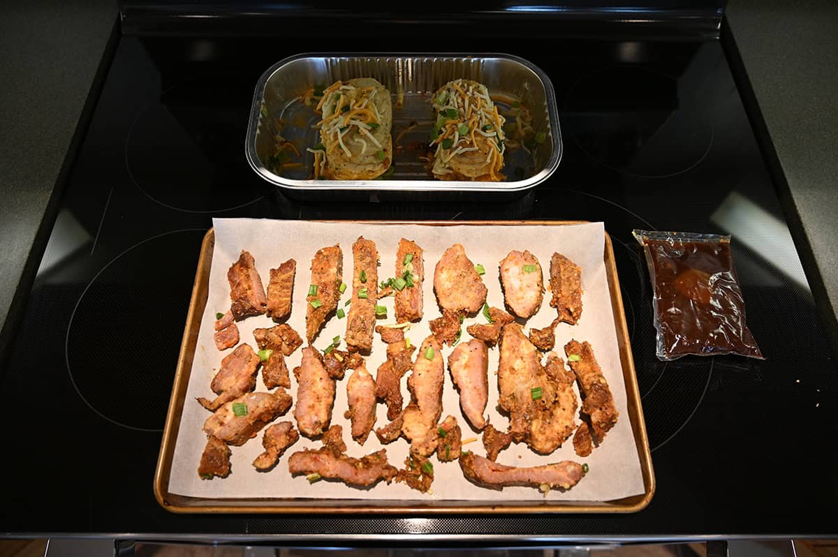 Top down image of rib ends served on a baking tray ready to be cooked and two baked potatoes in a tray ready to be cooked.