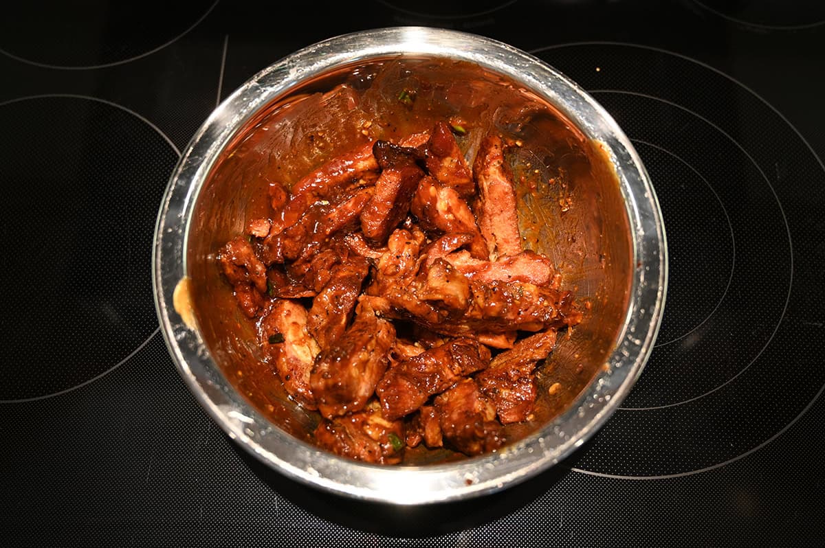 Image of ribs being tossed with sauce in a stainless steel bowl.