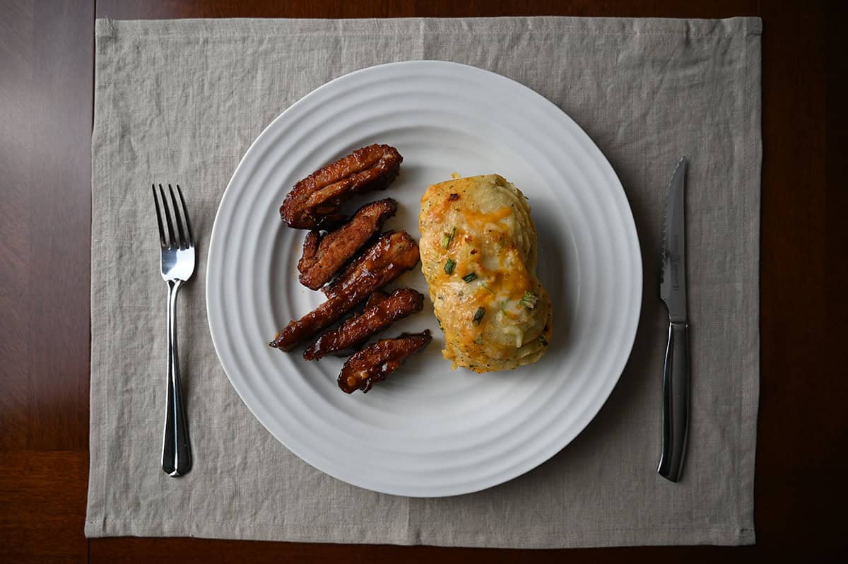 Top down image of one large baked potato served beside five rib ends on a white plate.