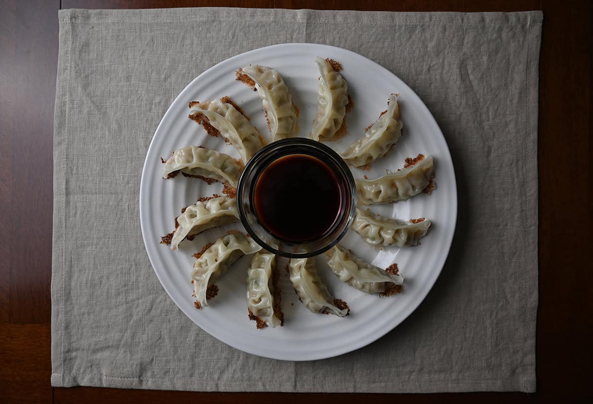 Image of gyoza served in a circular pattern on a plate with soy sauce in the middle.