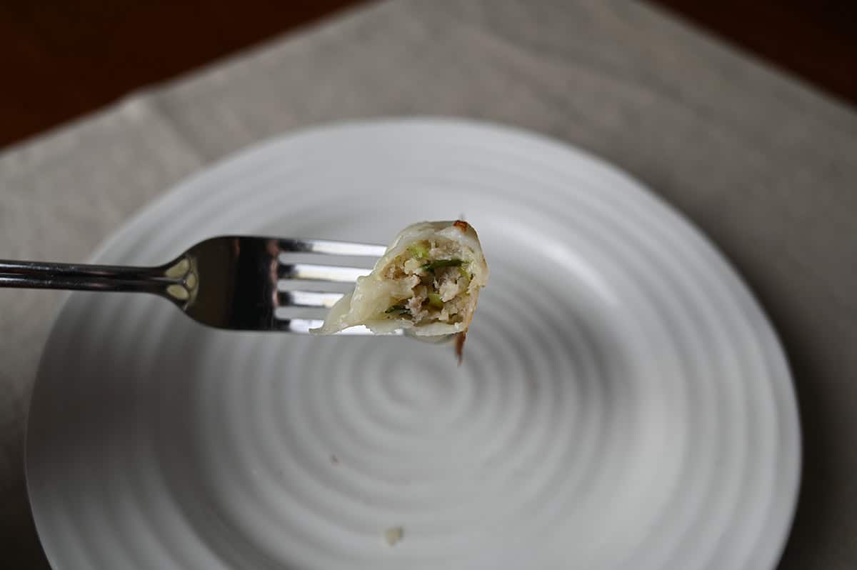 Closeup image of a fork with a gyoza on it with a few bites taken out of it so you can see the center.