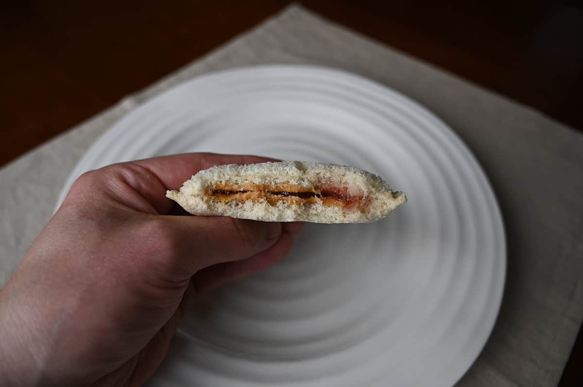 Image of a hand holding one Uncrustable close to the camera with a few bites taken out of it so you can see the peanut butter and jam center. 