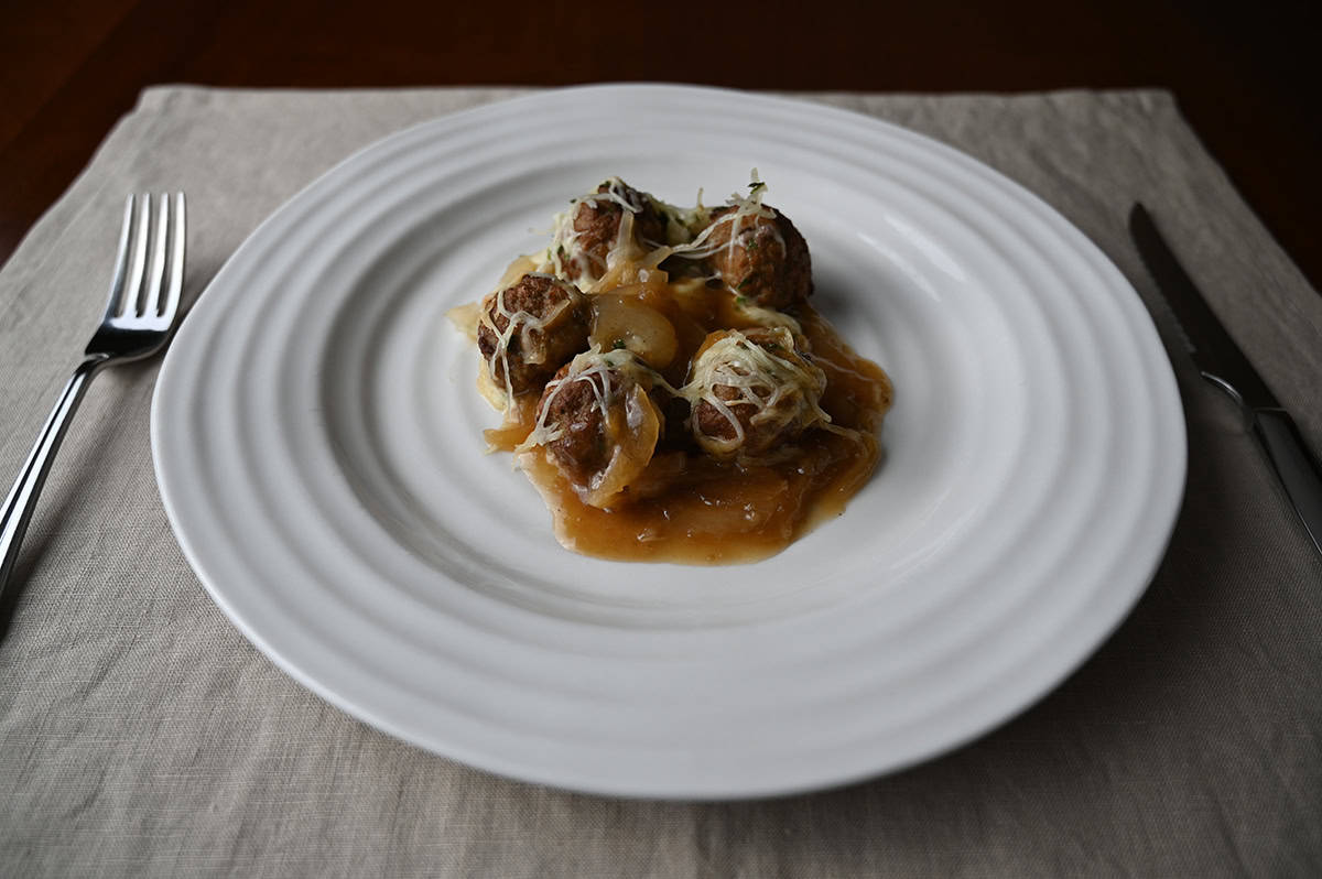 Closeup sideview image of a plate of five meatballs with cheese and onions on top of them served on a white plate.