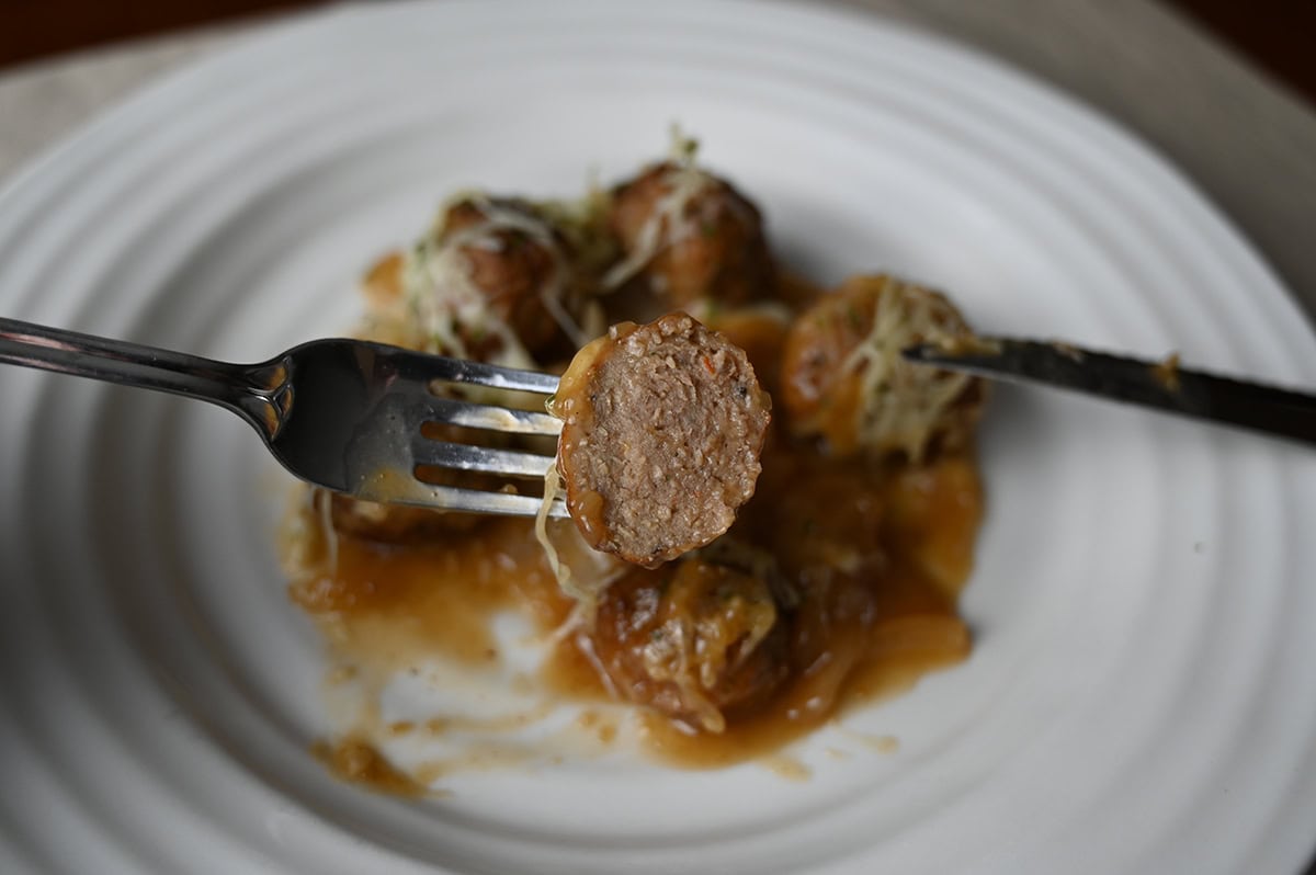 Closeup image of a fork with half a meatball on it close to the camera so you can see the inside of the meatball.