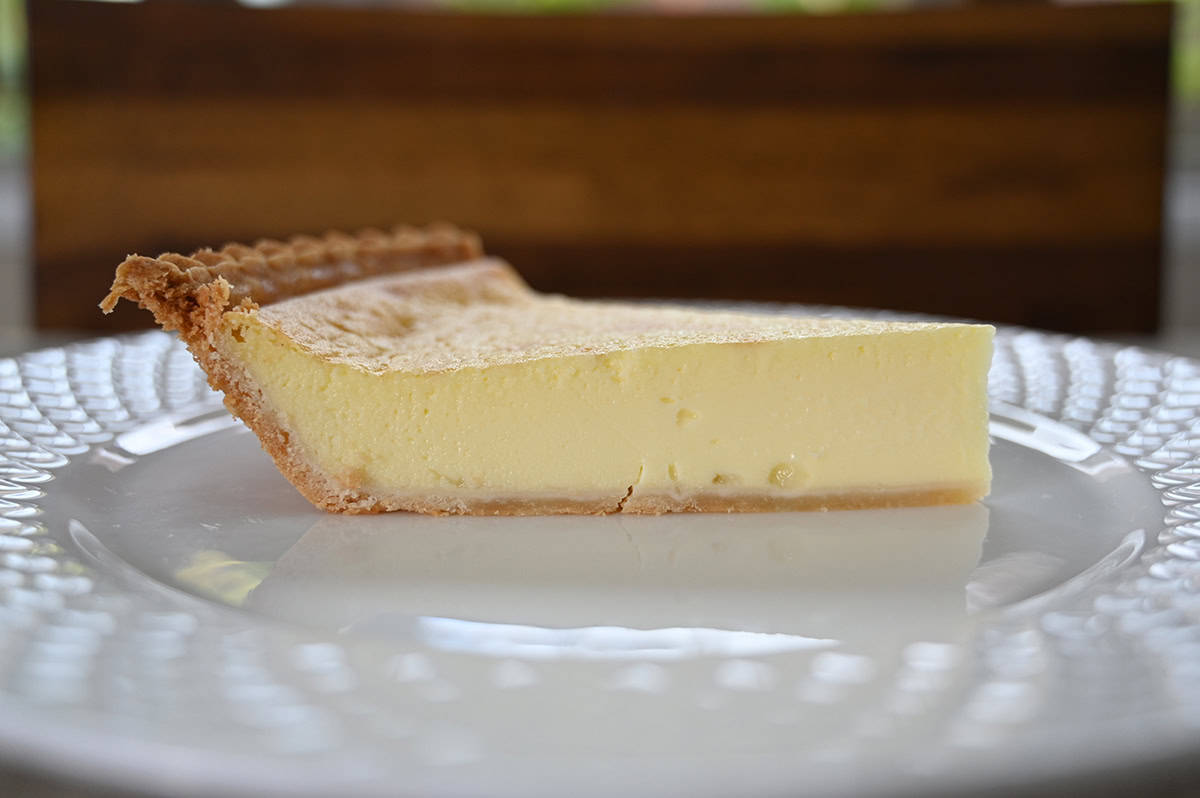 Closeup sideview image of a piece of custard pie on a white plate showing the depth of the pie and the custard filling.