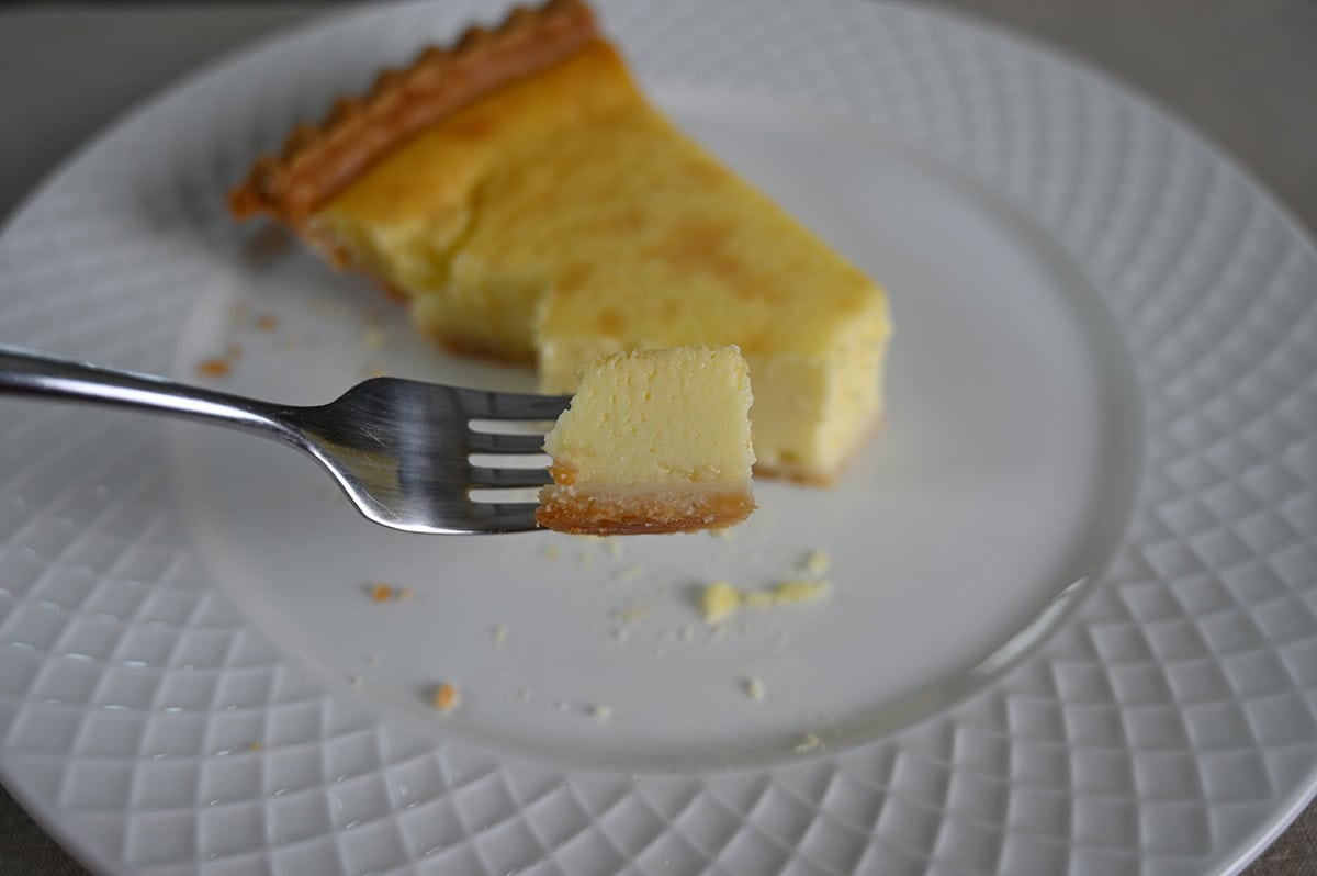 Closeup image of a fork with a bite of custard pie on it, in the background is a slice of custard pie.