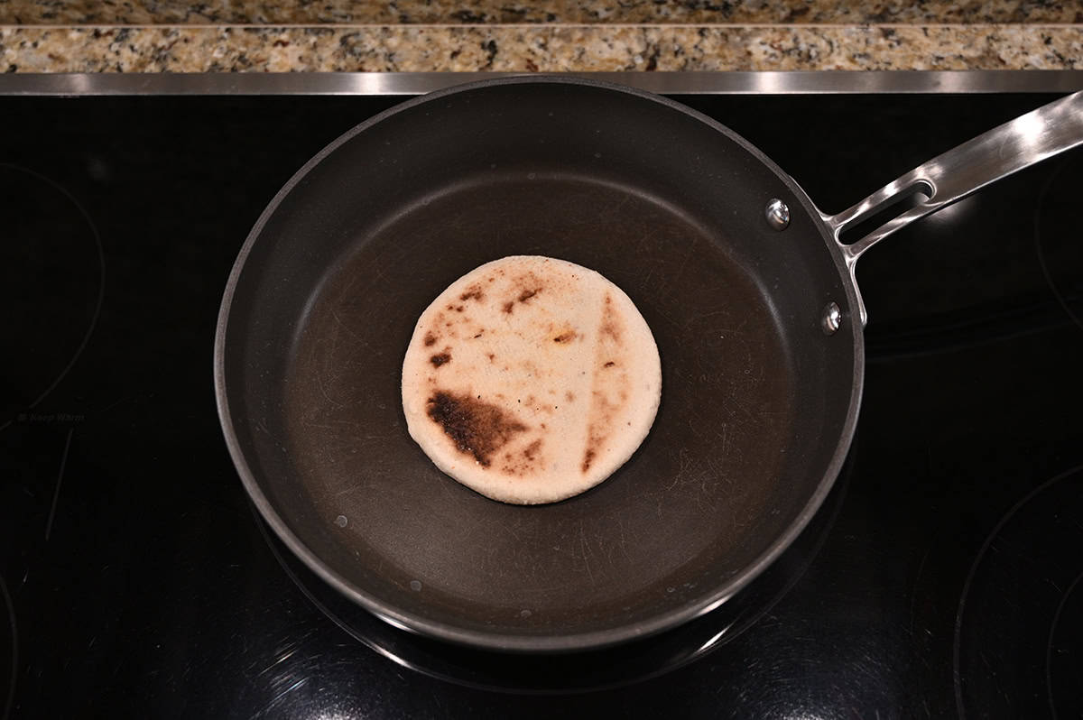 Top down image of one pupusa being cooked in a frying pan.