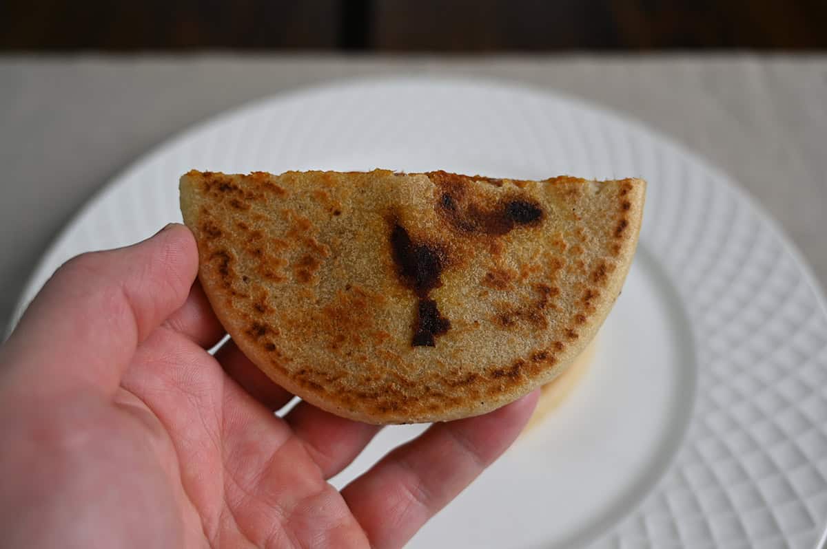 Image of a hand holding one pupusa that's been cut in half close to the camera.