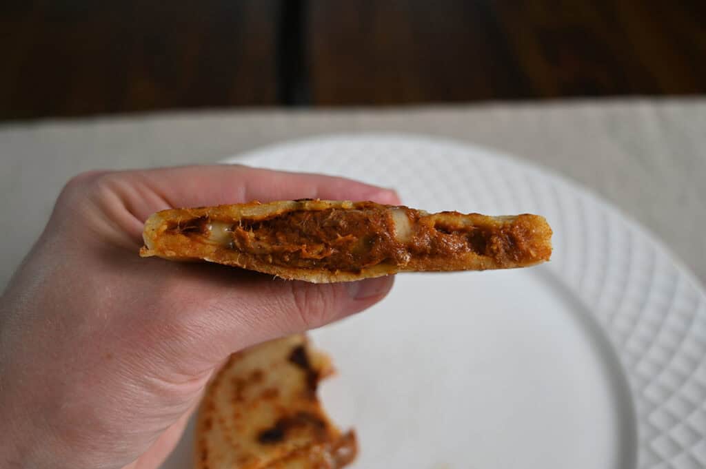 Image of a hand holding one pupusa close to the camera that's been cut in half so you can see the filling inside.