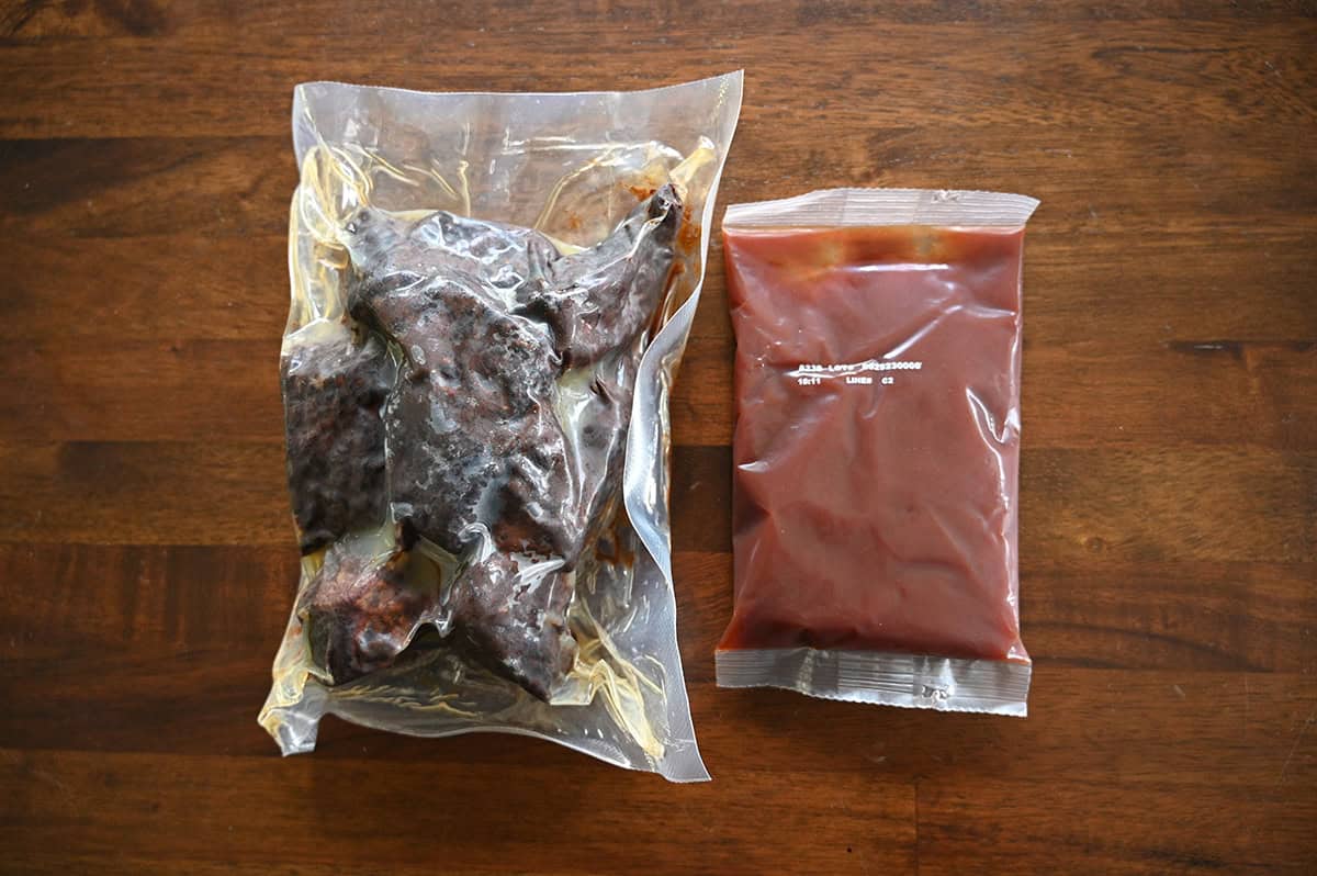 Top down image of one pouch of brisket burnt ends and one pouch of barbecue sauce sitting on a table unopened.