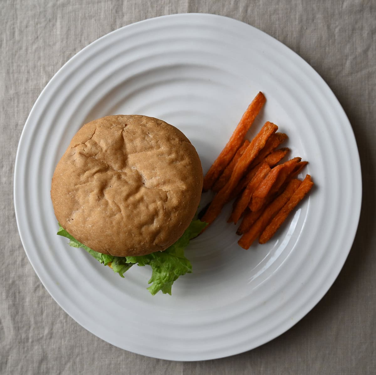 Image of a hamburger on a white plate beside a serving of fries.