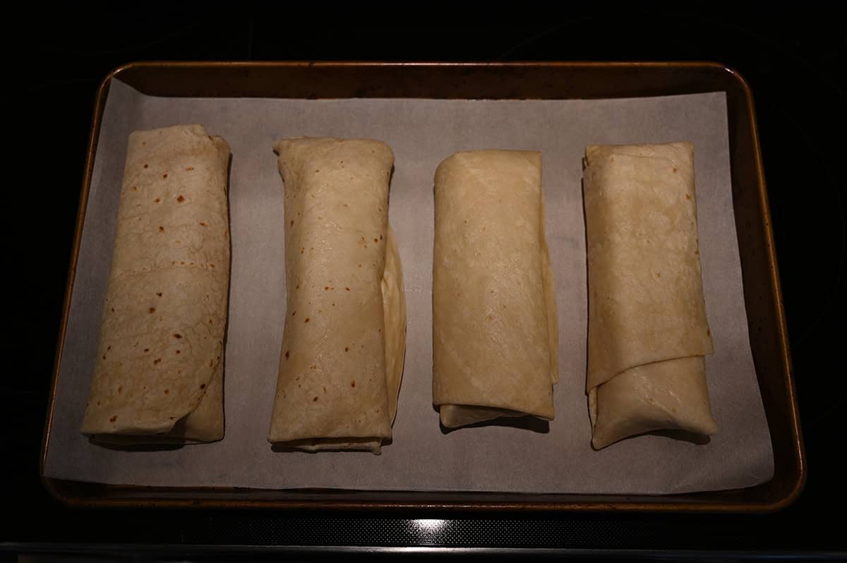 Image of four burritos on a baking tray lined with parchment paper before baking the burritos.