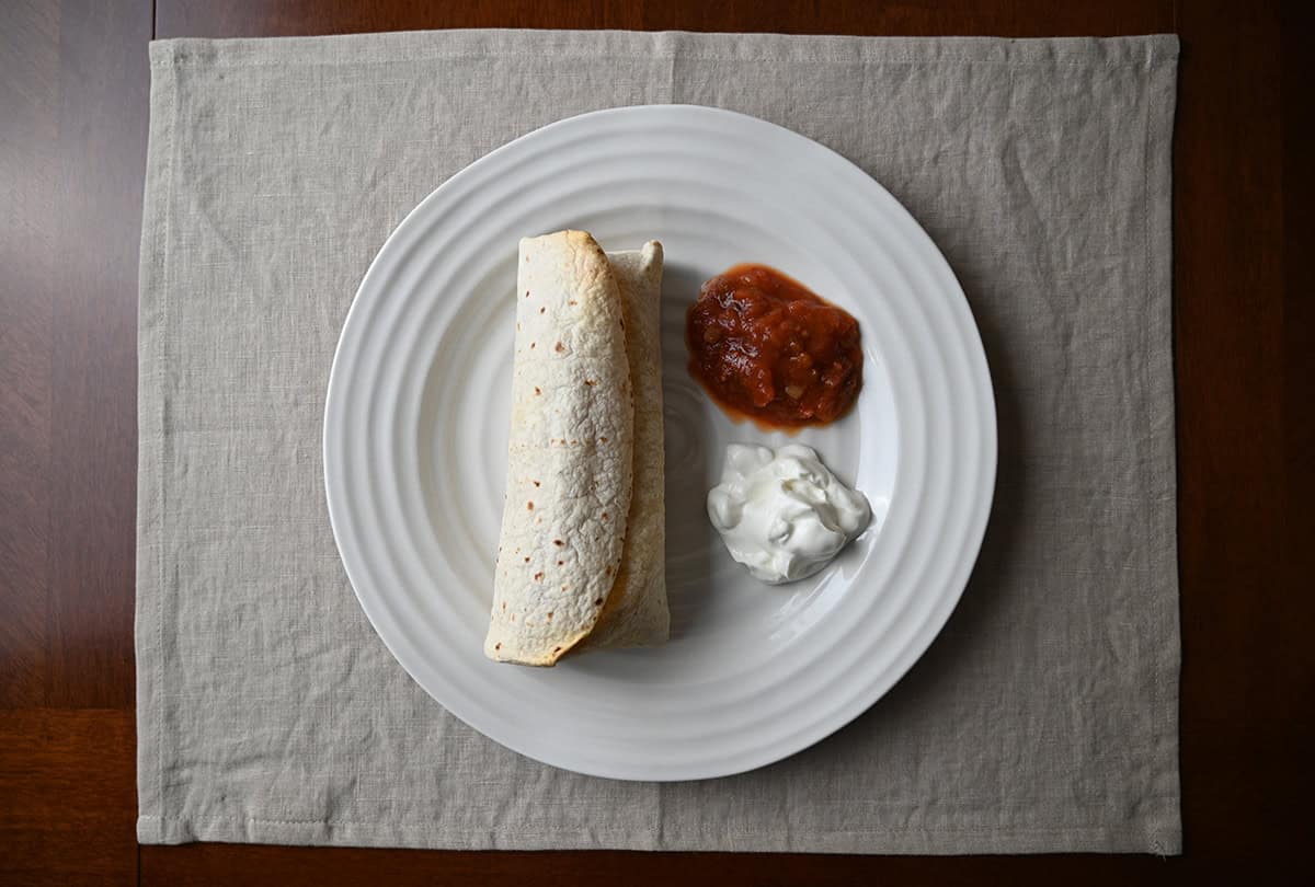 Image of a burrito served on a white plate beside sour cream and salad.