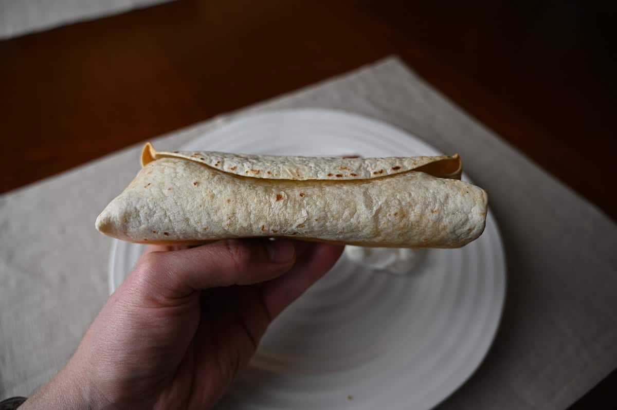 Image of a hand holding a burrito close to the camera on it's side so you can see how long and thick the burrito is.