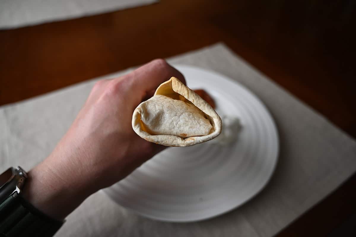 Image of a hand holding a burrito close to the camera before taking a bite of out of it.