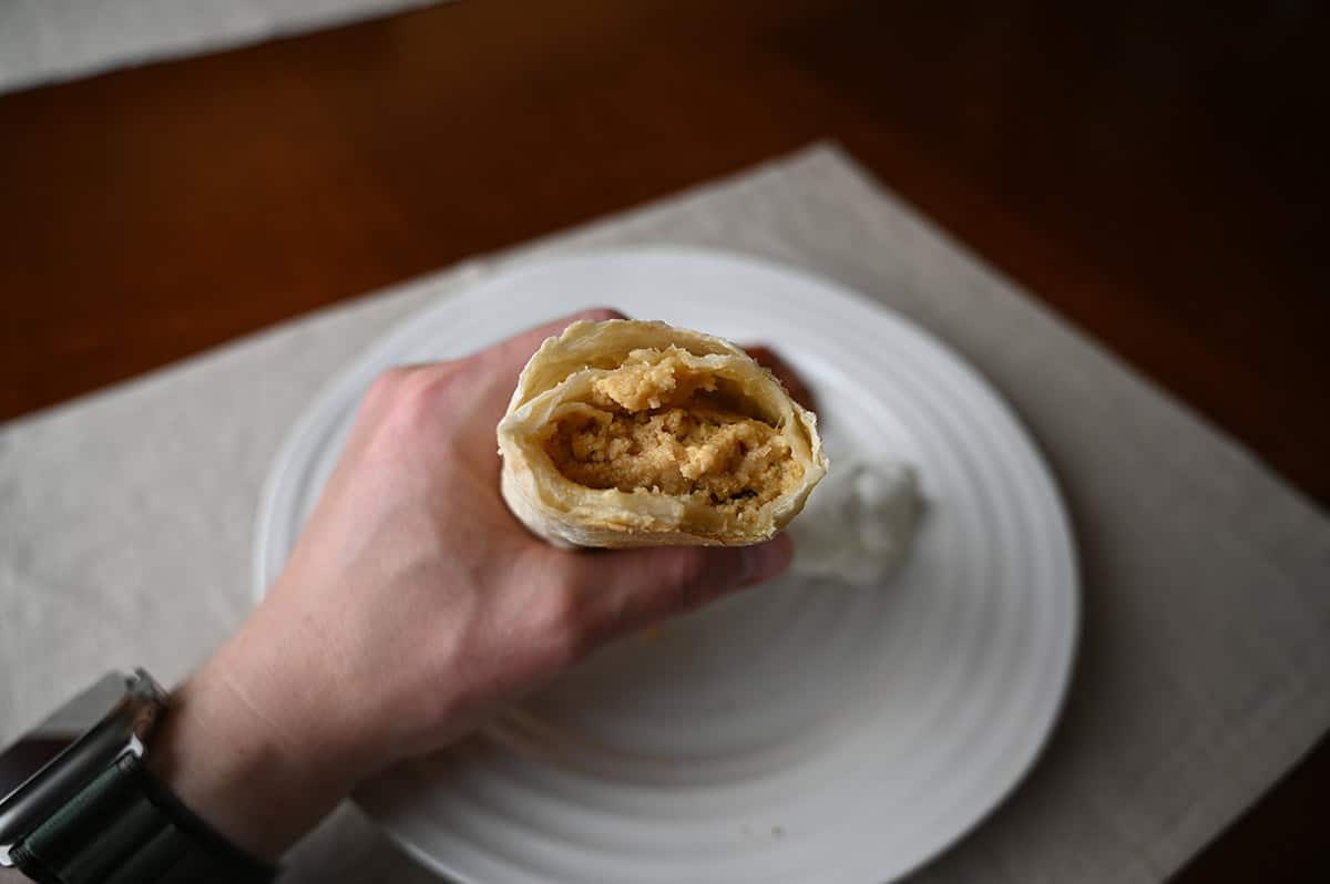 Image of a hand holding a burrito close to the camera with a few bites taken out of it so you can see the filling.