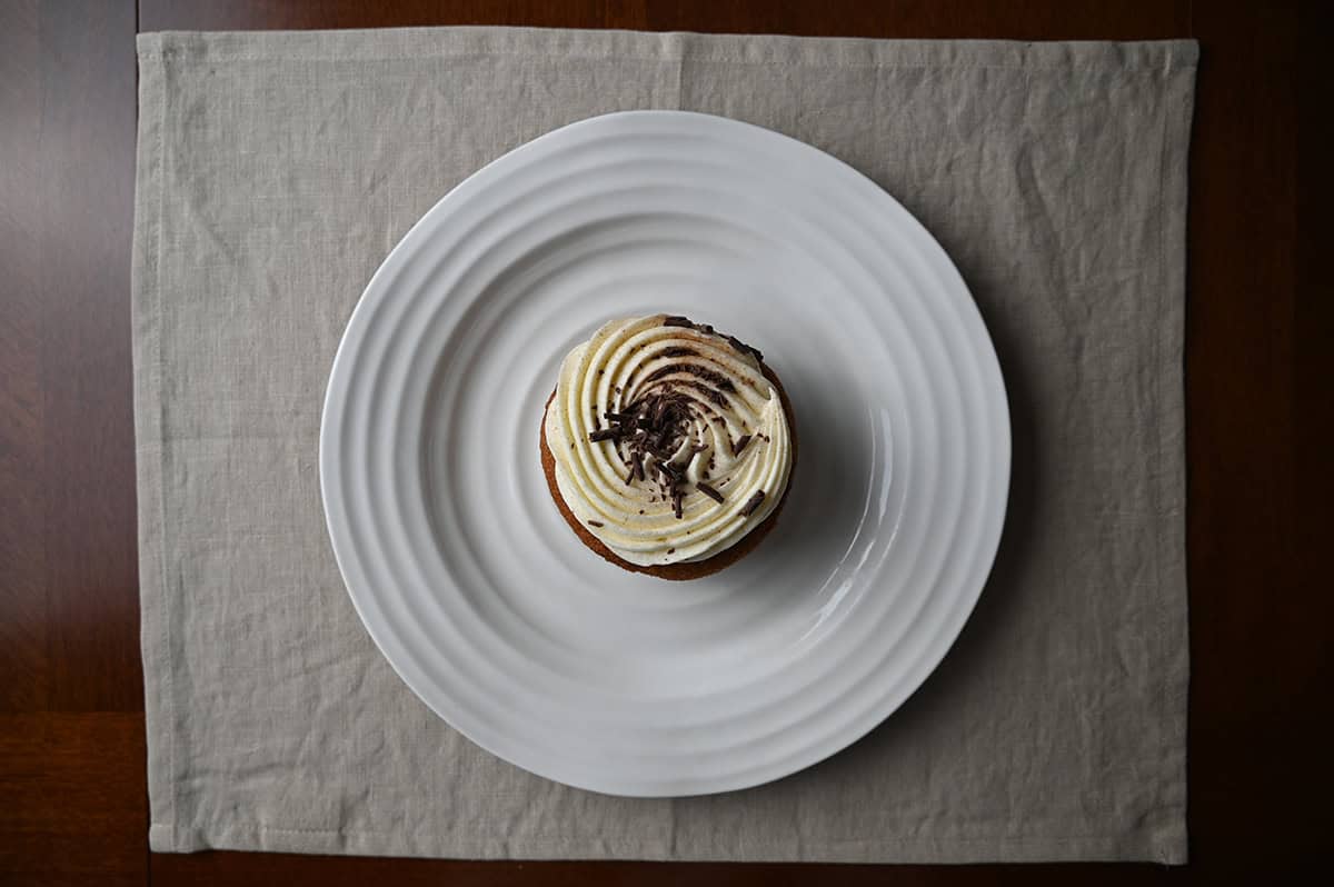 Image of one cinnamon roll mini cake served on a white plate with chocolate shavings on top.