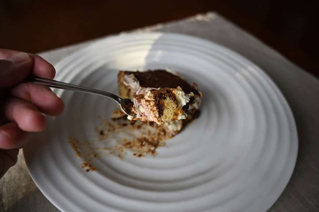 Image of a fork with a bite of Tiramisu Scoop Cake hovering over a plate with a slice 