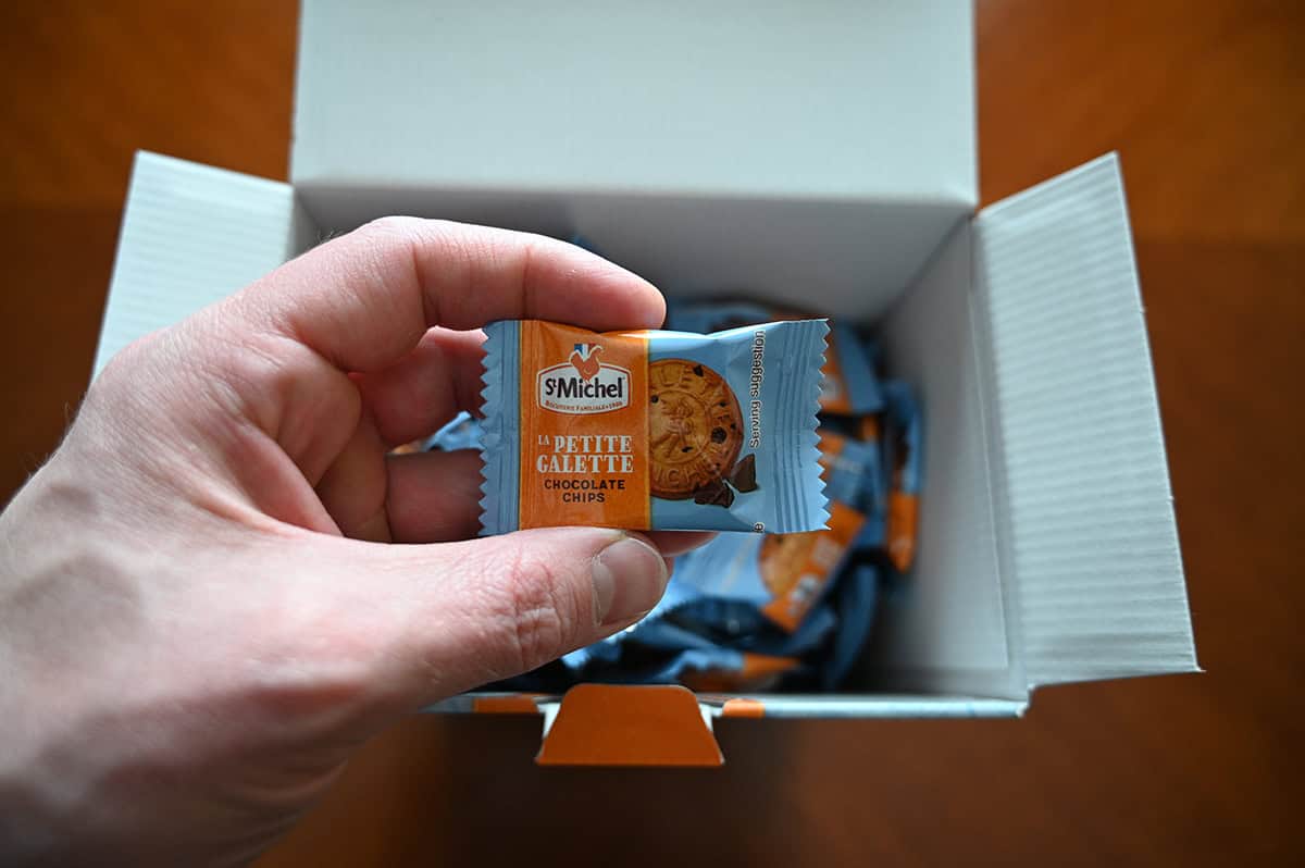 Image of an open box of cookies with a hand holding one individually wrapped cookie over the box.